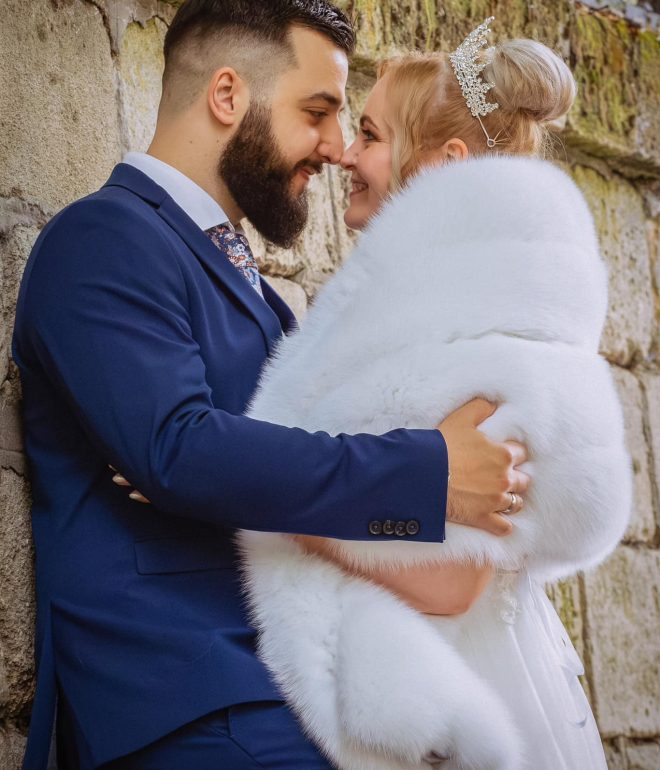 Esküvői fotó- és videózás – vőlegény mosolyogva nézi menyasszonyt elegáns bundában