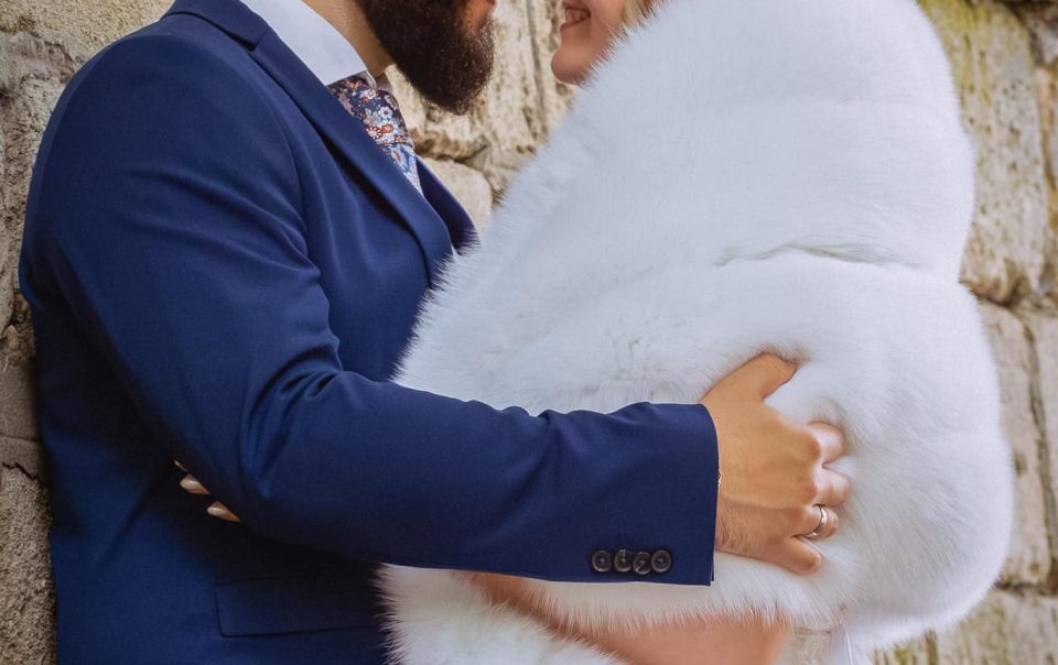 Esküvői fotó- és videózás – vőlegény mosolyogva nézi menyasszonyt elegáns bundában